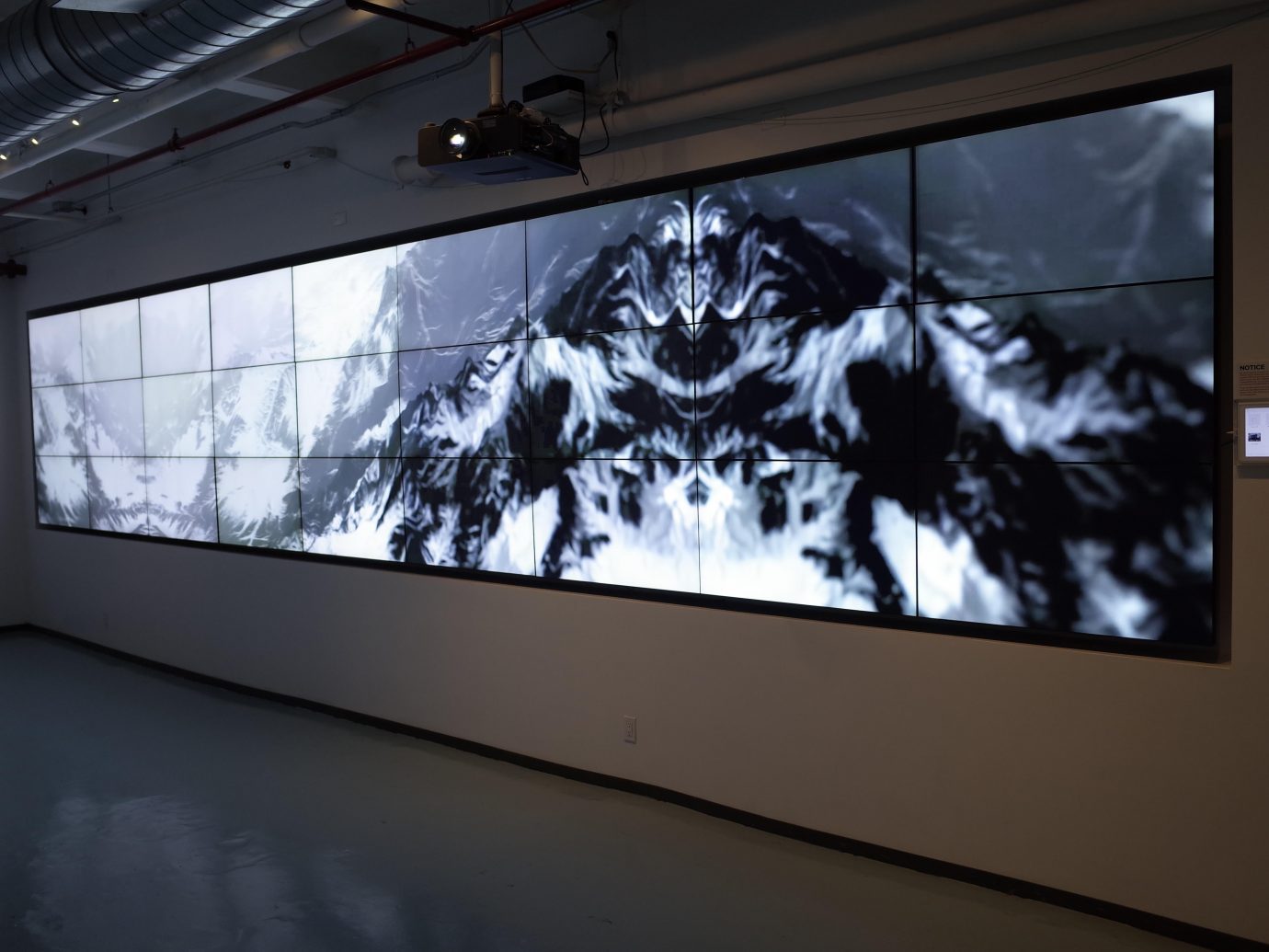 Modern, generative art installation displayed across multiple screens arranged side by side to form a single, large canvas. Mountain range.