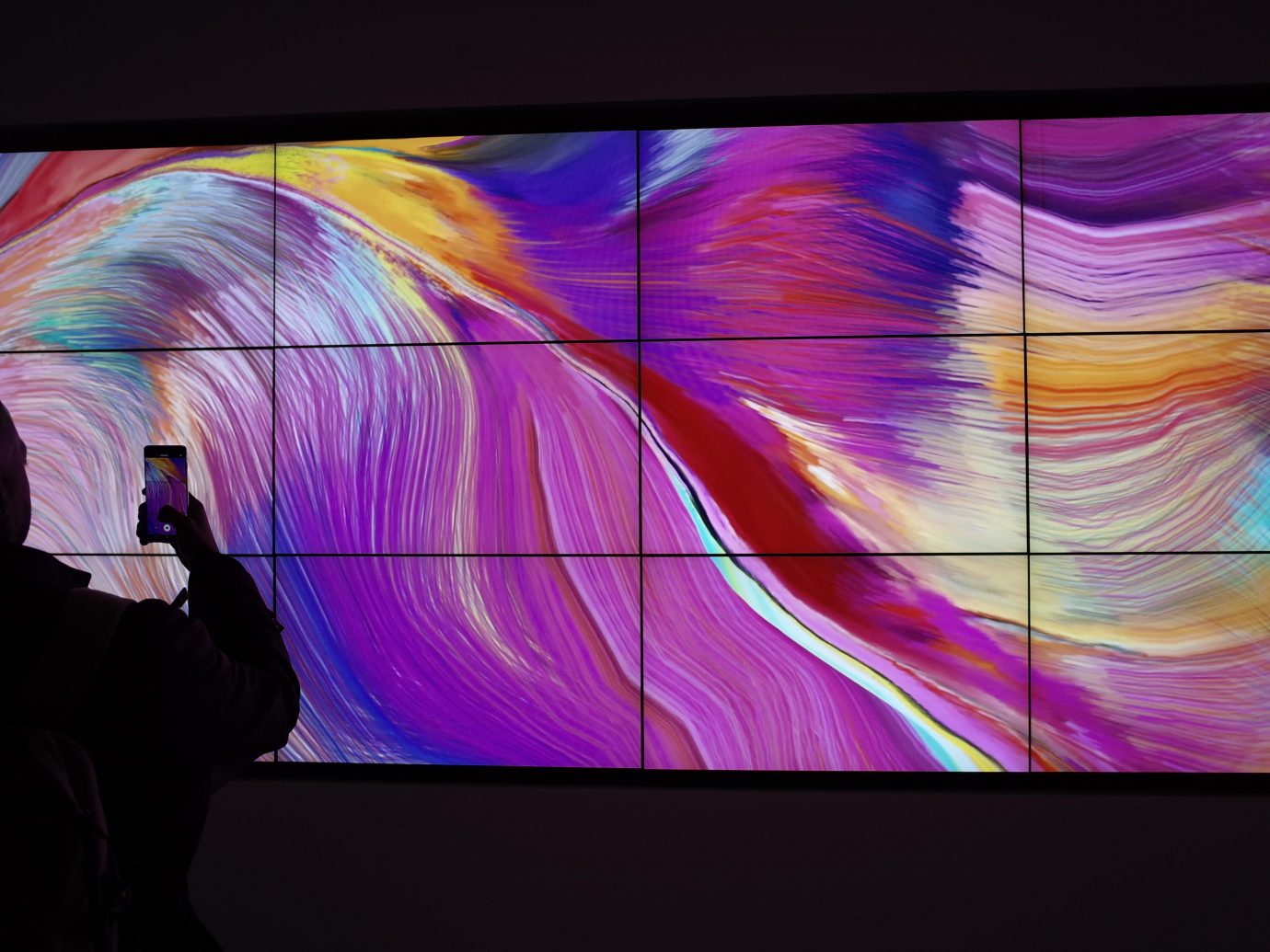 Modern, generative art installation displayed across multiple screens arranged side by side to form a single, large canvas.